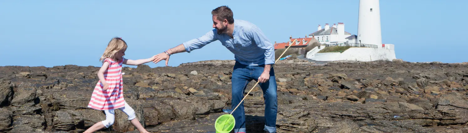 Klippen mit leuchtturm am Meer: Vater hilft seiner kleinen Tochter über eine Pfütze zu springen.