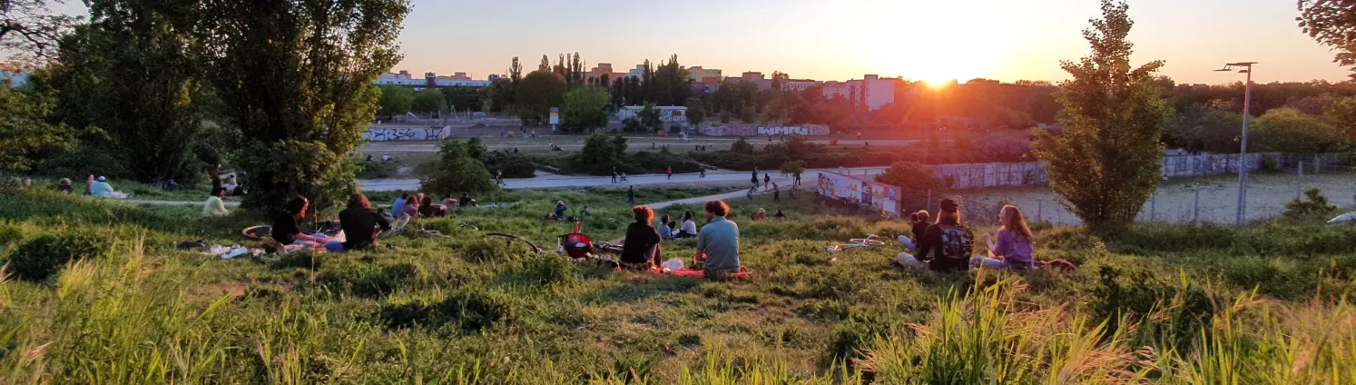 Menschen sitzen im Gras und betrachten den Sonnenuntergang im Berliner Mauerpark.